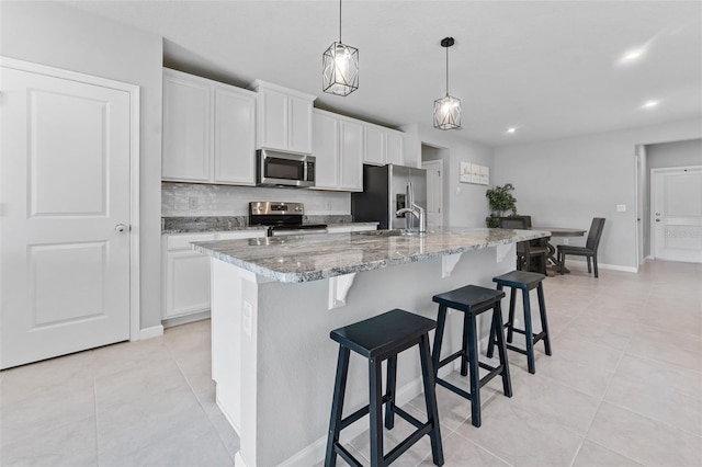 kitchen featuring decorative light fixtures, an island with sink, stainless steel appliances, decorative backsplash, and white cabinets