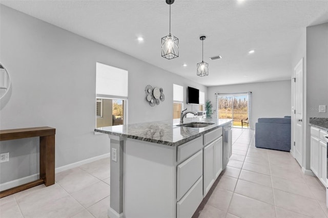 kitchen with sink, white cabinetry, decorative light fixtures, dark stone counters, and a kitchen island with sink