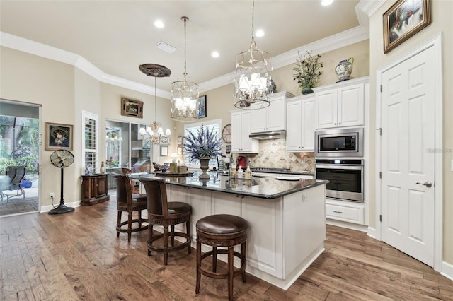 kitchen with a kitchen bar, decorative light fixtures, stainless steel appliances, a large island, and white cabinets