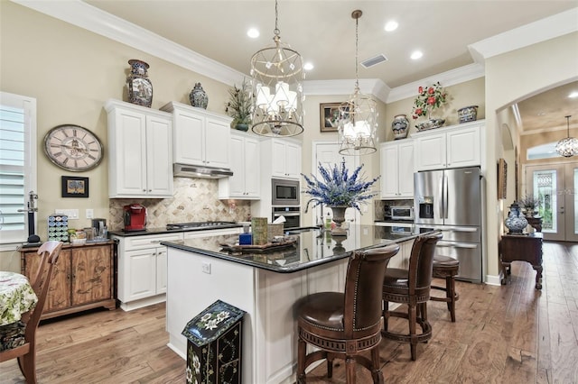 kitchen featuring white cabinetry, stainless steel appliances, decorative light fixtures, and a kitchen island with sink