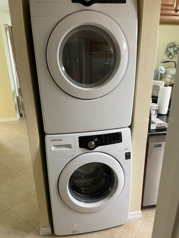 laundry area with stacked washer / drying machine and light tile patterned floors