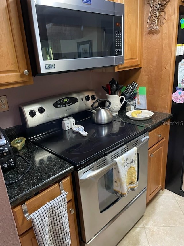 kitchen featuring appliances with stainless steel finishes, light tile patterned floors, and dark stone counters