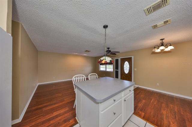 kitchen with decorative light fixtures, dark hardwood / wood-style floors, a kitchen island, a notable chandelier, and white cabinets