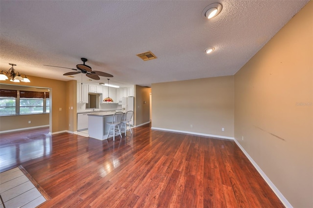 unfurnished living room featuring ceiling fan with notable chandelier, a textured ceiling, and dark hardwood / wood-style flooring