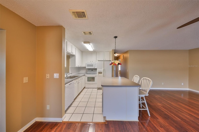 kitchen featuring white cabinetry, sink, a center island, white appliances, and light hardwood / wood-style flooring