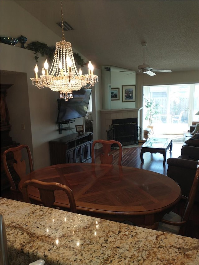 dining area with a tiled fireplace, vaulted ceiling, and ceiling fan