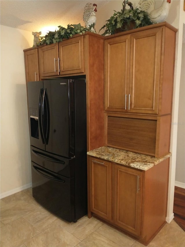 kitchen featuring black fridge with ice dispenser and light stone countertops