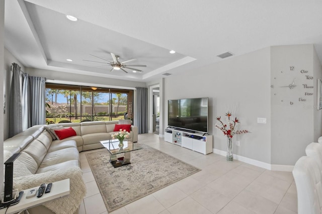 living room featuring ceiling fan, a tray ceiling, and light tile patterned floors