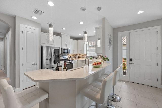 kitchen with sink, white cabinetry, stainless steel appliances, a kitchen bar, and decorative light fixtures