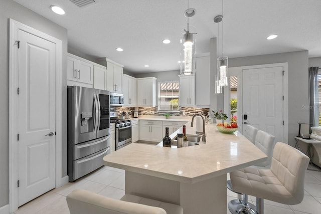 kitchen with a breakfast bar area, white cabinetry, appliances with stainless steel finishes, pendant lighting, and backsplash