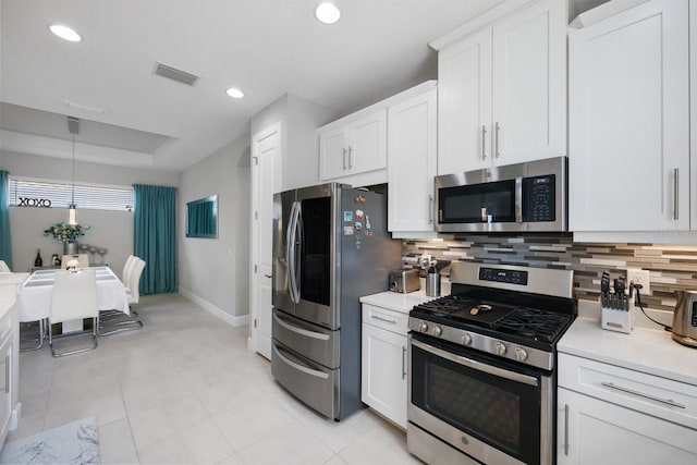 kitchen featuring light tile patterned flooring, appliances with stainless steel finishes, pendant lighting, white cabinets, and decorative backsplash