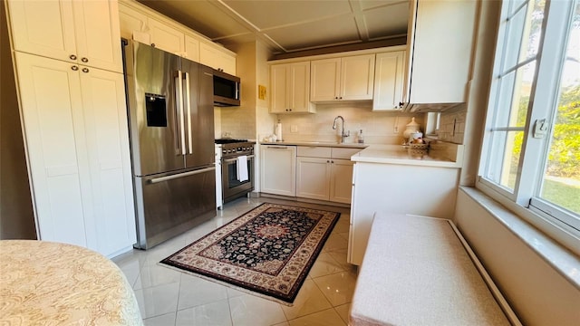 kitchen featuring sink, high end appliances, light tile patterned floors, white cabinets, and backsplash