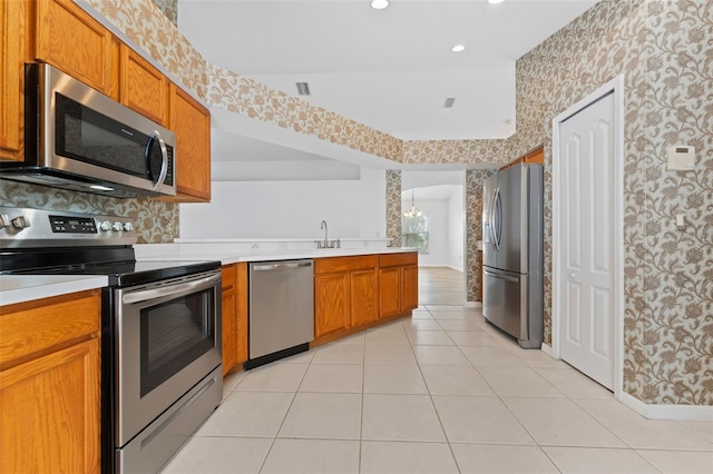 kitchen with appliances with stainless steel finishes, kitchen peninsula, sink, and light tile patterned floors