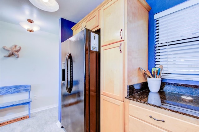 kitchen with dark stone countertops, light brown cabinetry, and black refrigerator with ice dispenser