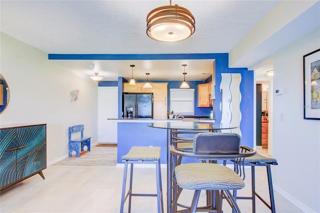 kitchen with black fridge with ice dispenser, a breakfast bar area, light brown cabinets, pendant lighting, and light hardwood / wood-style floors