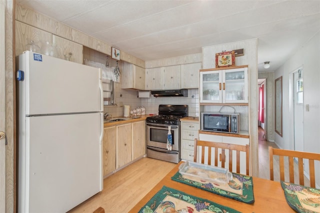 kitchen with light brown cabinetry, stainless steel gas range oven, white fridge, light hardwood / wood-style floors, and decorative backsplash