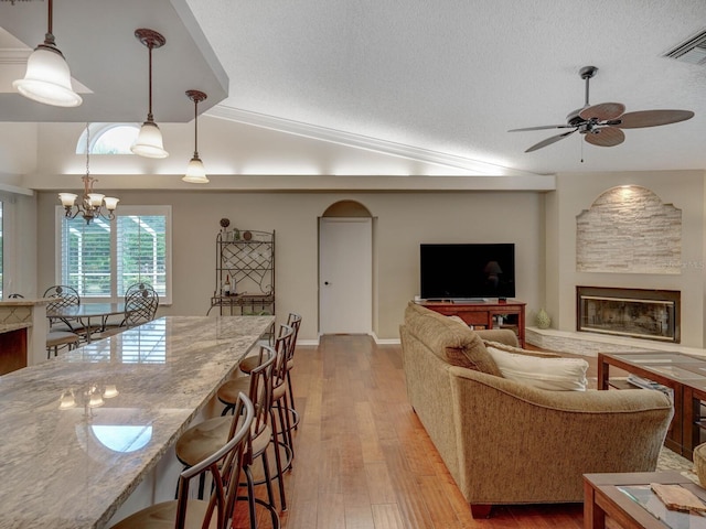 living room featuring lofted ceiling, ceiling fan with notable chandelier, a textured ceiling, and light wood-type flooring