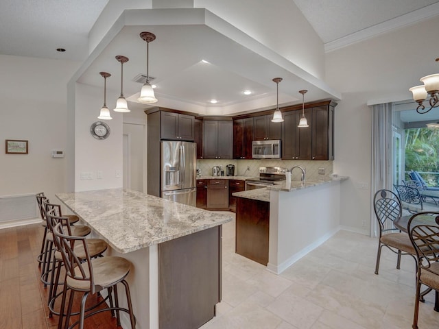 kitchen featuring appliances with stainless steel finishes, hanging light fixtures, dark brown cabinets, light stone countertops, and kitchen peninsula