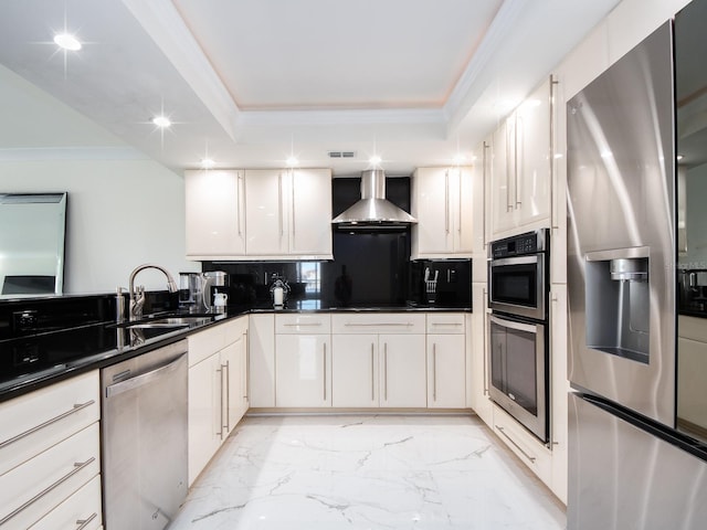 kitchen with wall chimney range hood, sink, white cabinetry, stainless steel appliances, and a raised ceiling