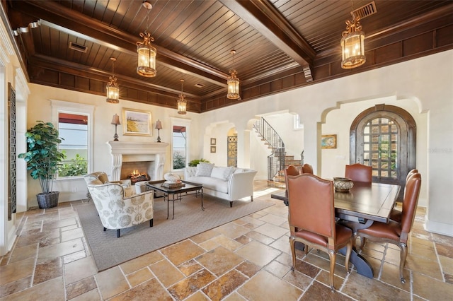 interior space with arched walkways, stone tile floors, wood ceiling, a lit fireplace, and beam ceiling