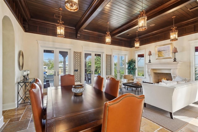 dining room with french doors, beam ceiling, stone tile flooring, wooden ceiling, and a lit fireplace