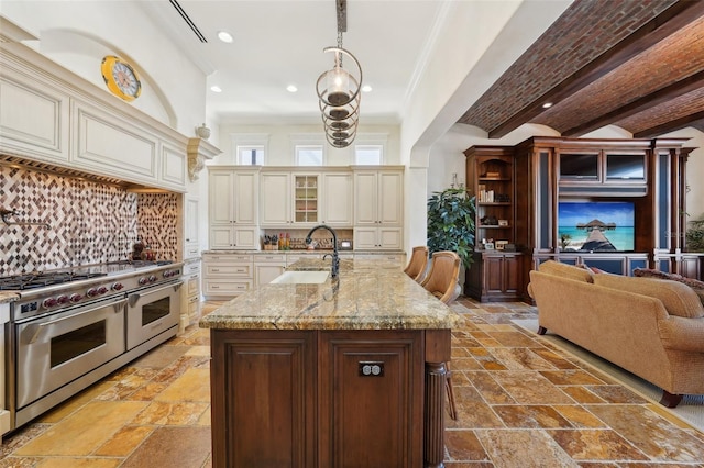 kitchen with glass insert cabinets, cream cabinetry, double oven range, pendant lighting, and a sink