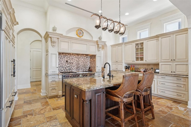 kitchen with stone tile floors, a center island with sink, glass insert cabinets, and a sink