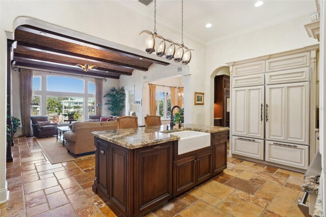 kitchen featuring stone tile floors, a sink, open floor plan, cream cabinetry, and an island with sink