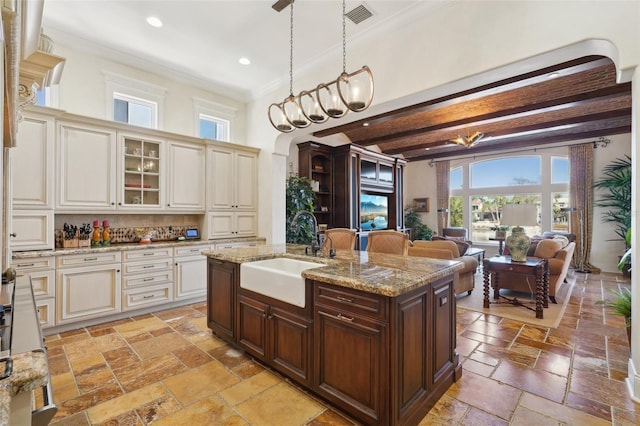 kitchen featuring visible vents, glass insert cabinets, decorative light fixtures, stone tile flooring, and a sink