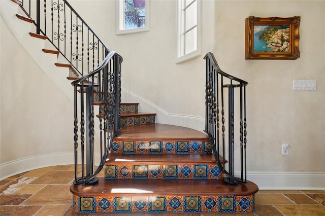 staircase featuring baseboards and stone tile floors