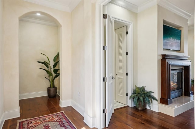 hallway featuring arched walkways, baseboards, dark wood finished floors, and crown molding