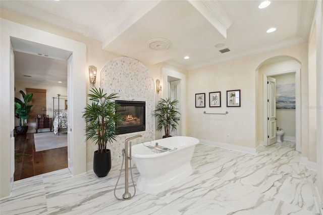 bathroom featuring a freestanding tub, baseboards, marble finish floor, ornamental molding, and a glass covered fireplace