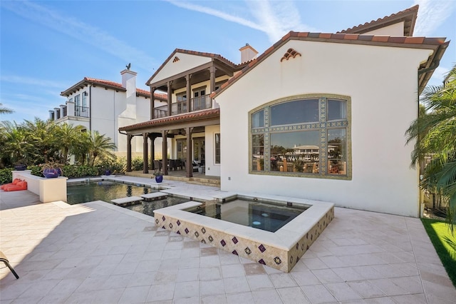 back of house featuring an outdoor pool, a patio, a balcony, and an in ground hot tub