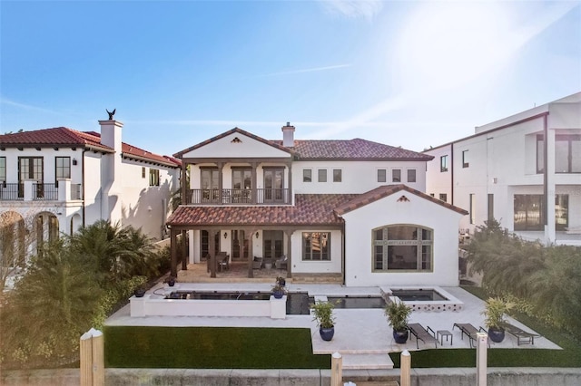 rear view of house with a patio, a tiled roof, a balcony, and stucco siding