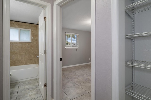 bathroom featuring tile patterned floors, a healthy amount of sunlight, a bathing tub, and a textured ceiling