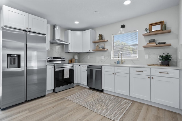 kitchen with wall chimney range hood, stainless steel appliances, sink, and white cabinets