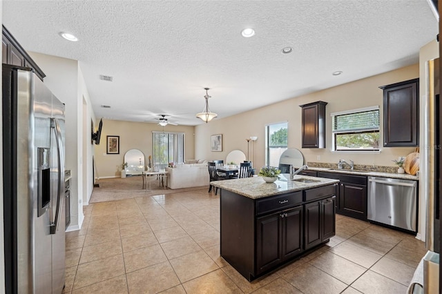 kitchen featuring hanging light fixtures, light tile patterned floors, a center island with sink, and appliances with stainless steel finishes