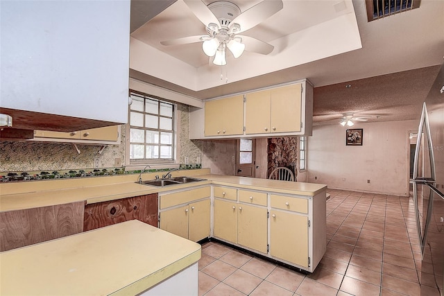 kitchen featuring sink, stainless steel fridge, a tray ceiling, light tile patterned flooring, and kitchen peninsula