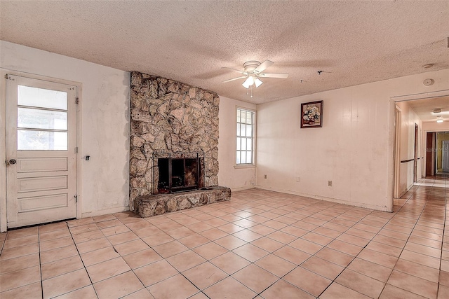 unfurnished living room with a stone fireplace, a textured ceiling, ceiling fan, and light tile patterned flooring