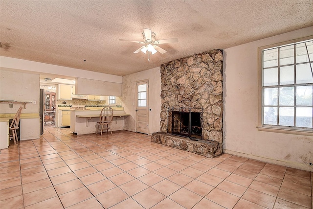 tiled living room with ceiling fan, a textured ceiling, and a fireplace