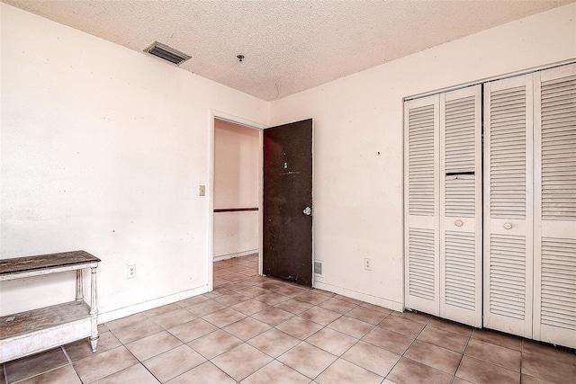 unfurnished bedroom with a closet, a textured ceiling, and light tile patterned flooring