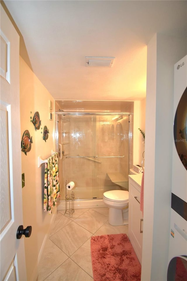 bathroom with stacked washer / drying machine, toilet, a shower with shower door, and tile patterned flooring