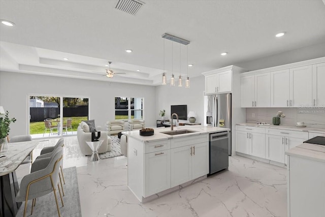 kitchen featuring pendant lighting, stainless steel appliances, white cabinets, and a center island with sink