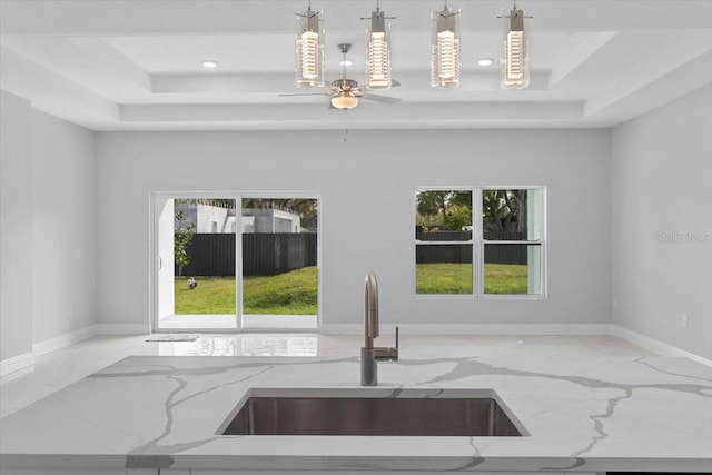 kitchen featuring sink, decorative light fixtures, light stone countertops, and a raised ceiling