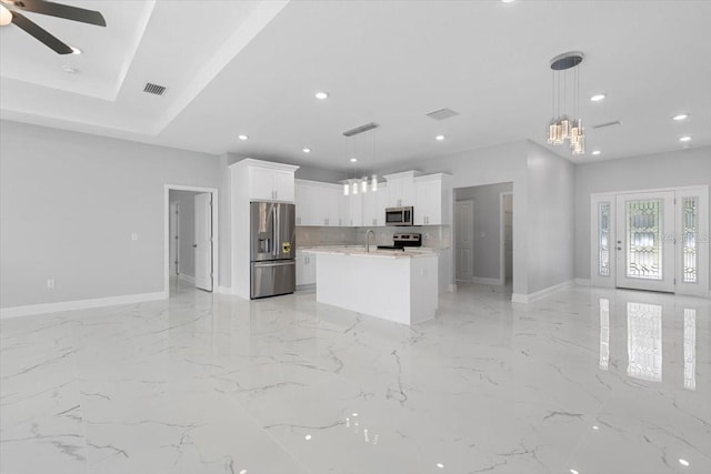 kitchen featuring sink, white cabinetry, stainless steel appliances, an island with sink, and decorative light fixtures