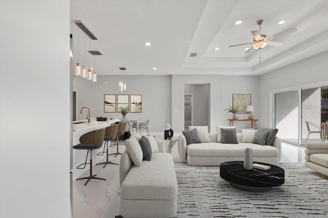 living room featuring ceiling fan, a raised ceiling, and sink