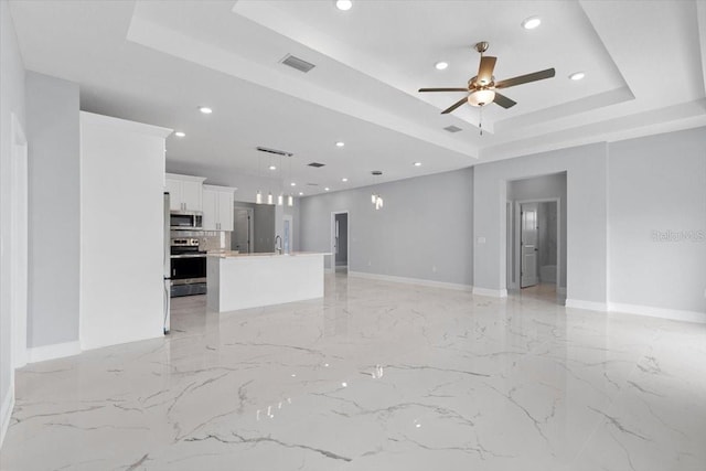 unfurnished living room with ceiling fan and a tray ceiling