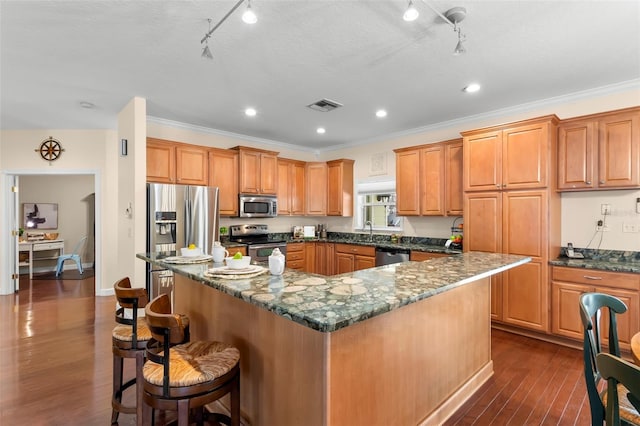 kitchen with stainless steel appliances, a kitchen island, dark hardwood / wood-style floors, and dark stone countertops