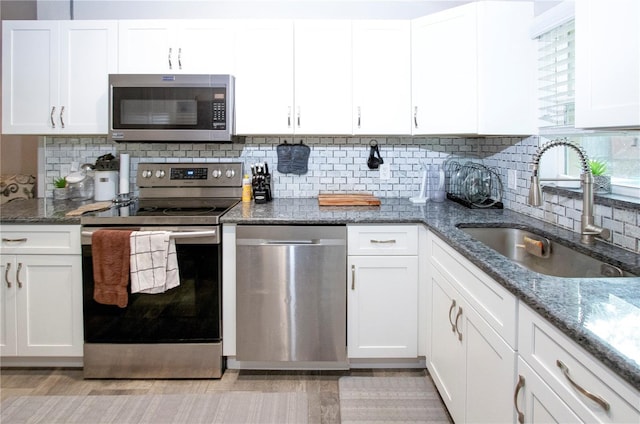 kitchen featuring white cabinetry, appliances with stainless steel finishes, dark stone counters, and a sink