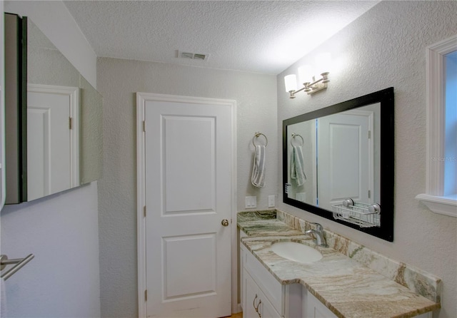 bathroom with a textured wall, visible vents, a textured ceiling, and vanity